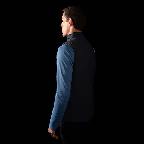 a fit photo of a person wearing the mens ascent stretch vest with 60g primaloft gold insulation in colorway DEEP SPACE with a mens pursuit longsleeve in MINDFUL BLUE underneath