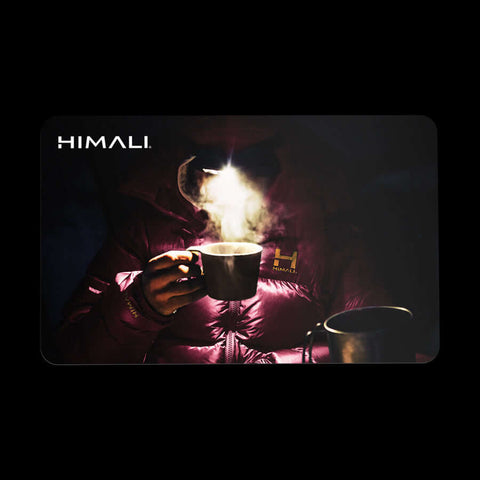 a gift card with the image of a person in a Monk Red HIMALI Altitude Parka. The person is drinking hot tea out of a mug and the steam is illuminated by their headlamp.